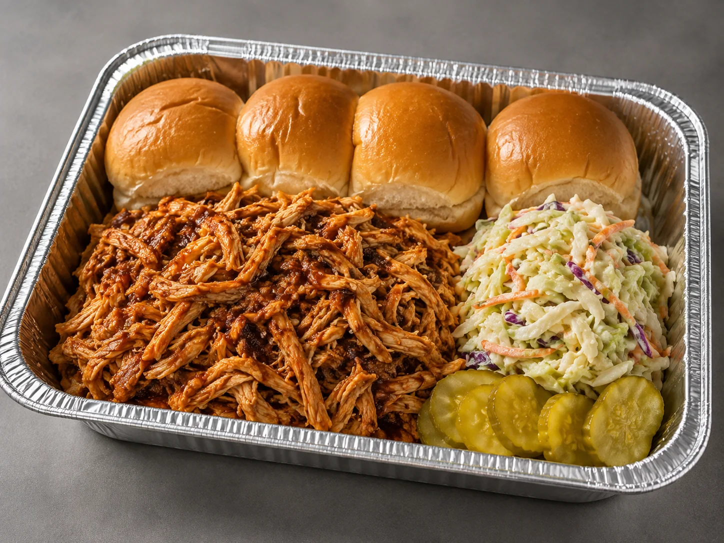 BBQ Pulled Chicken Sliders Family Bundle with saucy pulled chicken, slider rolls, coleslaw and roasted sweet potato wedges in an aluminum tray
