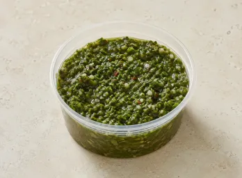 Chimichurri in a clear takeout sauce cup.