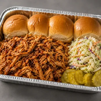 BBQ Pulled Chicken Sliders Family Bundle with saucy pulled chicken, slider rolls, coleslaw and roasted sweet potato wedges in an aluminum tray