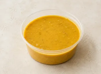 Almond Coconut Curry in a clear takeout sauce cup.