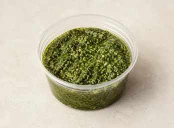 Homemade Pesto in a clear takeout sauce cup.