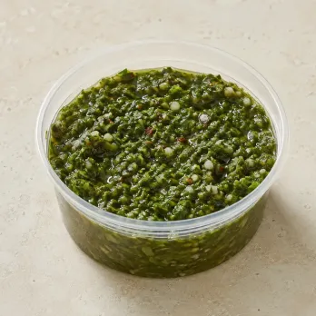 Chimichurri in a clear takeout sauce cup.